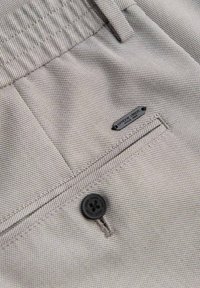 Pantalon en tissu texturé gris clair avec un bouton noir, une passants de ceinture et une petite étiquette métallique portant l'inscription « ombre dept. since 1985. »
