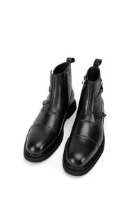 Botines de cuero negro con puntera puntiaguda, paneles laterales texturizados, inserciones elásticas y hebillas decorativas a los lados.