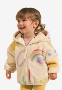 Veste en polaire avec capuche, de couleur crème, ornée de motifs multicolores incluant un arc-en-ciel, fermeture éclair et texture douce.