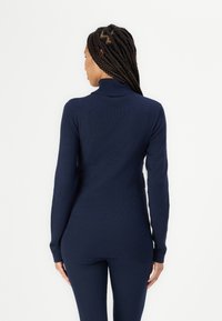Maglione a collo alto aderente di colore blu navy. Tessuto a coste, maniche lunghe e orlo posteriore leggermente allungato. Realizzato in materiale morbido ed elastico.