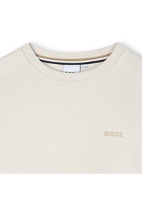 Μπέζ μπλουζάκι με στρογγυλή λαιμόκοψη, φτιαγμένο από λείο ύφασμα. Διαθέτει το λογότυπο "BOSS" σε ανοιχτό καφέ στο στήθος και αντίθετο σχέδιο στην εσωτερική λαιμόκοψη.