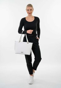 Zwarte geribbelde longsleeve top gecombineerd met high-waisted zwarte broek en witte sneakers. Een grote witte tote bag met gouden hardware accenten.
