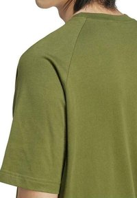 Camiseta de manga corta en verde oliva con un corte relajado, textura suave y mangas raglán distintivas. Diseño simple sin patrones.