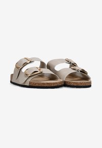 Sandali beige con due ampie cinghie, ciascuna dotata di una fibbia dorata. Suola in sughero testurizzato con un fondo in gomma nera per una migliore aderenza.