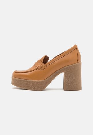 Zapatos de plataforma de cuero color marrón claro con punta redondeada, que cuentan con un tacón grueso texturizado y detalles de costura visibles en el embozo.