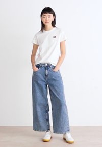 Witte katoenen t-shirt met een klein logo, gecombineerd met wijdvallende blauwe denim jeans. Draag het met witte sneakers met gele zolen.