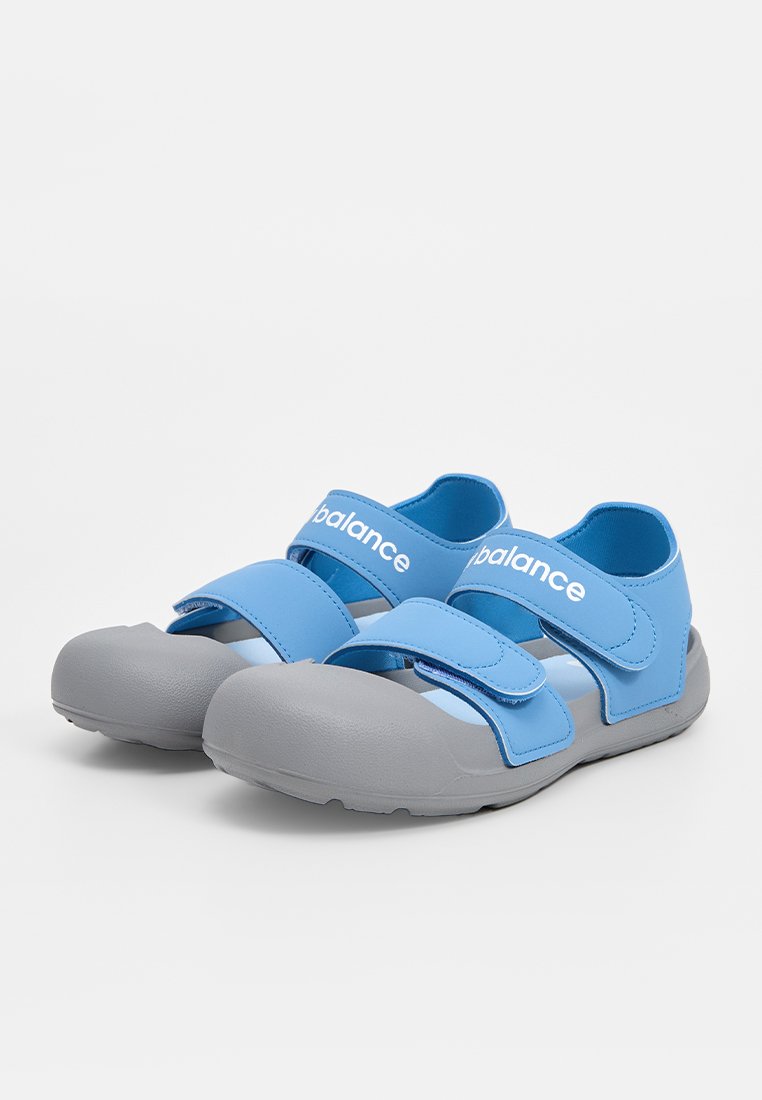Sandalias azules y grises con dos correas de Velcro, una textura suave y un diseño de puntera redondeada. Presenta un logo en la correa.