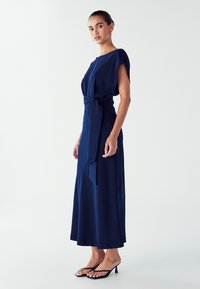 Mornarsko plava haljina do članaka, slobodnog kroja, kratkih rukava i sa detaljem uvezanog struka. Glatka tkanina s mekom teksturom.