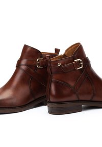 Brown leather ankle boots featuring a rounded toe, side buckle detail, textured finish, and a low stacked heel.