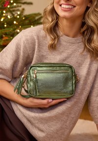 Žalia metalinė per petį nešama rankinė su užtrauktuku, tekstūruota paviršiumi, auksinėmis detalėmis ir kutų akcentais. Kompaktiška stačiakampio formos.