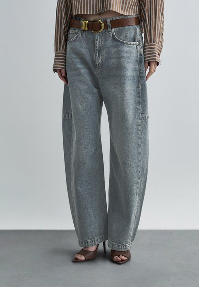 Jean en denim gris à jambes larges avec une texture délavée, doté d'une ceinture en cuir marron avec une boucle en or. Tissu lisse et design décontracté.