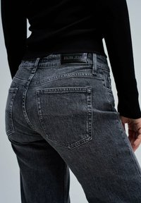 Jeans de mezclilla gris de talle alto con una textura desgastada, bolsillos traseros y una etiqueta negra que dice "SALSA JEANS" en la cintura.