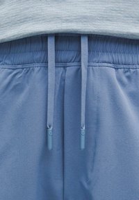 Blå atletiske shorts med en glat tekstur, der har en snor i taljen og elastisk linning. Detaljerne inkluderer endekapper på snorene.