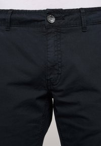 I chinos in cotone nero presentano una chiusura a bottone, passanti per cintura e una parte frontale piatta. Il tessuto ha una texture liscia con dettagli di cucitura sottili.