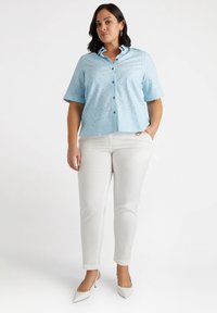Camisa de botones azul claro con mangas cortas y pequeños detalles; combinada con pantalones ajustados blancos y tacones puntiagudos blancos.