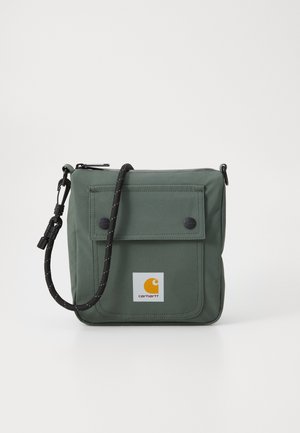 Small square green shoulder bag with front flap pocket, black adjustable cord strap, and Carhartt logo patch on pocket.