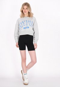 Szürke, cropped kapucnis pulóver kék "Joyful League" felirattal, fekete biker shortssal párosítva. A modellen fehér sportcipő és csíkos zokni található.