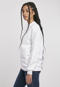 Felpa bianca a girocollo con maniche lunghe, vestibilità rilassata e polsini a costine. Indossata con jeans blu scuro, caratterizzati da una texture liscia.