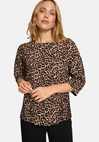 Bluse mit Leopardenmuster, drei Viertel langen Ärmeln, rundem Ausschnitt und lockerer Passform. Weicher Stoff mit strukturiertem Muster, kombiniert mit schwarzen Hosen.
