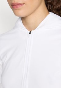 Bijela zip-up hoodie napravljena od glatkog materijala, s prednjim rajsferšlusom i prikladnom kapuljačom. Dizajn je minimalistički bez dodatnih uzoraka.