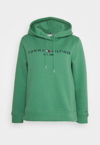 Zelená mikina Tommy Hilfiger s kapucí a šňůrkami, vyšívaným logem a emblémem vlajky na hrudi a malou vlajkou na manžetě levého rukávu.