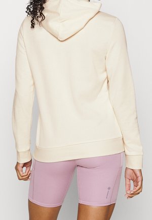 Sweat à capuche couleur crème avec capuche à cordon, associé à un short de vélo rose clair. Tissu doux, coupe décontractée et poignets côtelés.