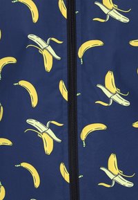 Navy stof met een herhalend patroon van gele bananen, met een zichtbare zwarte rits die verticaal over het midden loopt.