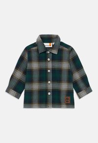 Chemise en flanelle à carreaux verts et gris avec des manches longues, un col pointu et des boutons blancs ; elle présente un logo en cuir marron en bas.