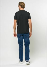 Juodas medvilninis marškinėliai trumpomis rankovėmis, suapvalintu iškirpimu, derinami su mėlynais džinsais ir baltais sportbačiais. Paprastas, kasdienis dizainas.