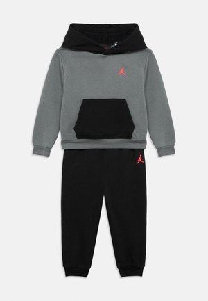 Grau-schwarzer Kapuzenpullover mit einer Fronttasche, kombiniert mit schwarzen Jogginghosen. Beide sind mit roten Jordan-Logo-Akzenten versehen. Weicher, lässiger Stoff.