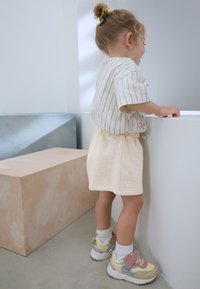 Chemise à manches courtes rayée, jupe beige à taille élastique, et baskets multicolores avec des accents roses et bleus. Textures lisses, coupe décontractée.