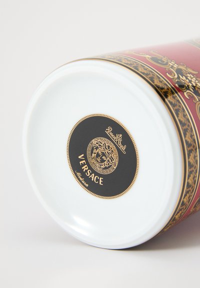 Okrągły porcelanowy pojemnik z czerwonym spodem, ozdobiony złoto-czarnym wzorem, z czarną etykietą z złotym logo Meduzy i napisem Versace.