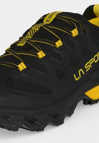 Schwarzer und gelber La Sportiva Wanderschuh mit robuster Sohle, gelben Schnürsenkeln und verstärktem Zehenbereich für Outdoor-Aktivitäten.