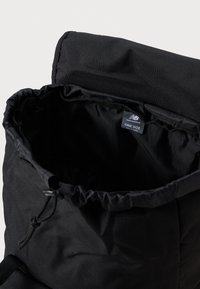 Bolsa negra con cordón hecha de un tejido duradero, con un interior suave y una etiqueta de logo que dice "TALLA ÚNICA". Diseño sencillo y funcional.