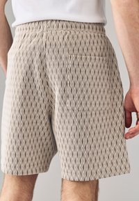 Beige korte broek met een diamantpatroon, elastische tailleband en een achterzak. Gemaakt van gestructureerde stof, knielengte ontwerp.