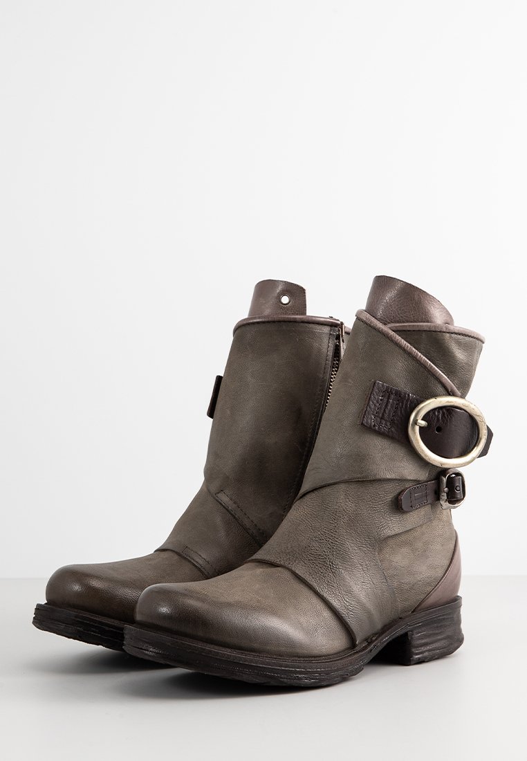 Bottines en cuir olive avec une finition usée, accents marron, fermeture éclair latérale, et détail décoratif en métal avec anneau et sangle.