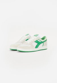 Weiße und grüne Sneakers mit einem Obermaterial aus Wildleder, perforierter Zehenpartie, grünen Akzenten und einer Gummisohle. Die Schnürsenkel sind weiß und der Schuhkragen ist gepolstert.