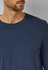 Marineblaues Langarm-T-Shirt mit Rundhalsausschnitt, das ein strukturiertes Paneel über der Brust und glatten Stoff am Rest aufweist.