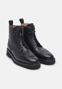 Stivaletti neri in pelle con finitura texture, dettagli brogue, design con lacci e linguette; caratterizzati da una suola in gomma robusta.