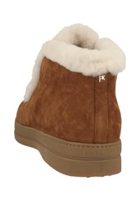 Stivale alla caviglia in suede marrone con colletto in finta pelliccia bianca, suola in gomma e dettaglio del logo dorato "PK" di lato. Texture morbida e forma arrotondata.