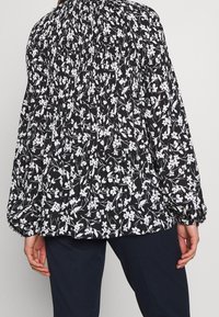 Floral-patterned blouse with a black background, white flowers, gathered neckline, and balloon sleeves. Soft fabric and relaxed fit.