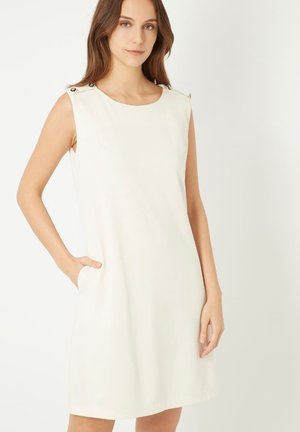 Vestido sin mangas de color crema con escote redondo, bolsillos laterales y botones decorativos plateados en los hombros. Tejido suave y ligero.