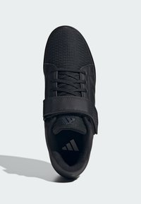 Scarpa sportiva nera con tomaia texturizzata, chiusura con lacci e strap in velcro. Include dettagli con logo e un colletto imbottito per il comfort.