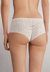 Lace hipster ondergoed in het wit, met ingewikkelde bloemmotieven, golvende randen en een zachte textuur, ontworpen voor volledige bedekking.