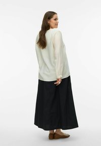 Blouse blanche texturée à manches longues associée à une jupe noire. La blouse est ample, tandis que la jupe est longue jusqu'à la cheville et fluide. Ballerines marron.