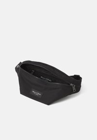 Juodas audinio fanny pack'as su užtrauktuku pagrindiniame skyriuje ir mažu priekinio užtrauktuko kišeniu. Su logotipo užtaisu ir reguliuojama dirželiu.