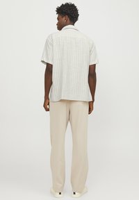 Camicia a maniche corte grigia chiaro a righe con una vestibilità comoda, abbinata a pantaloni beige a gamba larga e sneakers bianche, che mostrano elementi di design semplici.