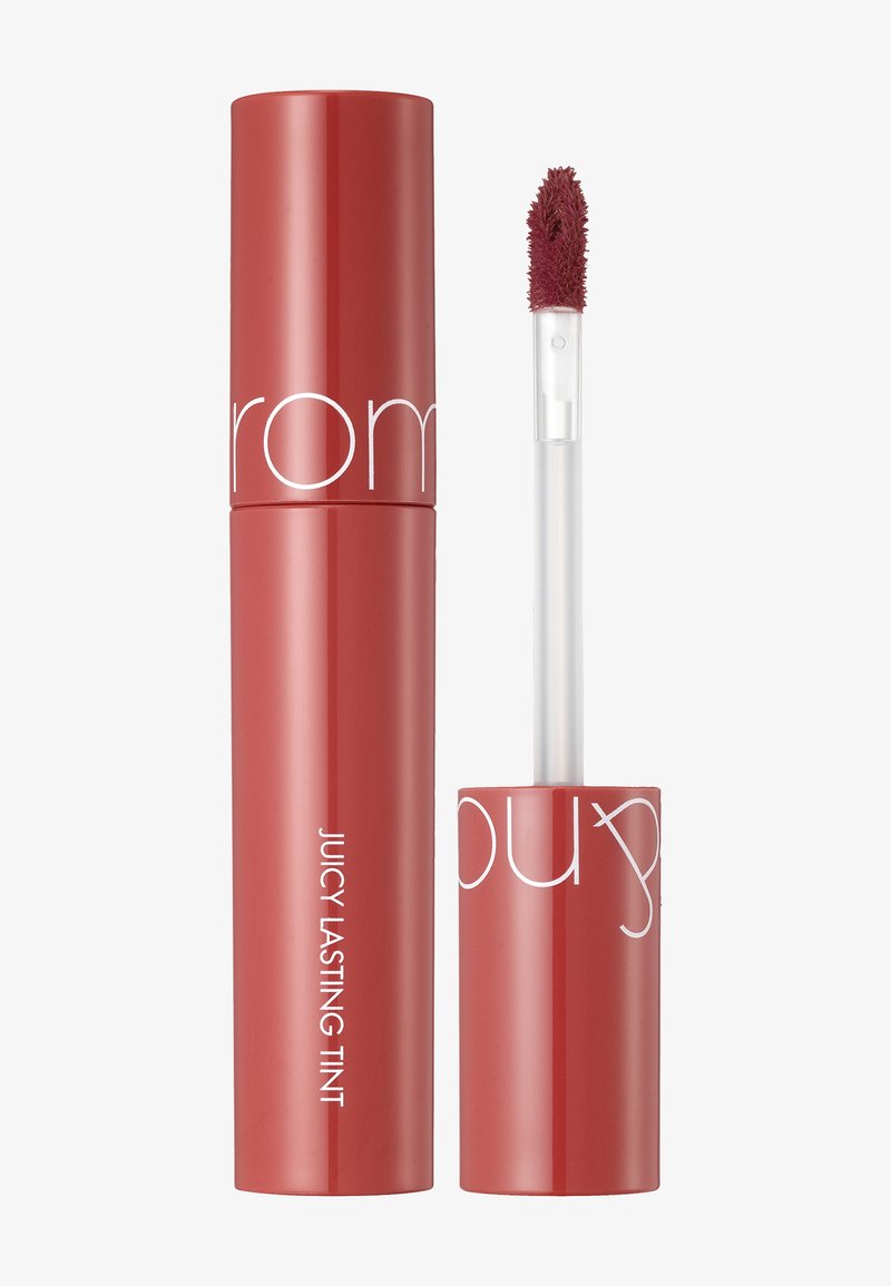 Teinte à lèvres liquide rouge dans un tube cylindrique avec une finition brillante. Applicateur texturé attaché. L'étiquette indique "Juicy Lasting Tint".