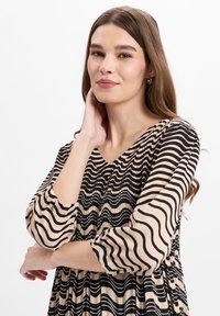 Langarmige jurk van lichtgewicht stof, met een V-hals, zwarte en beige golfpatronen, en geplooide details bij de taille.