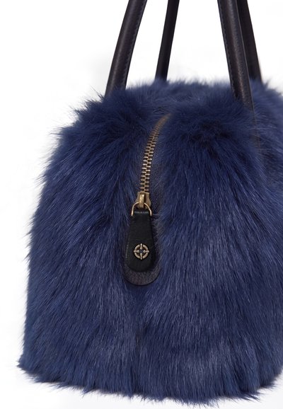 Sac à main en fourrure bleu foncé avec tirette de fermeture éclair en cuir noir et poignées, avec une fermeture éclair métallique visible et un emblème décoratif sur la tirette.